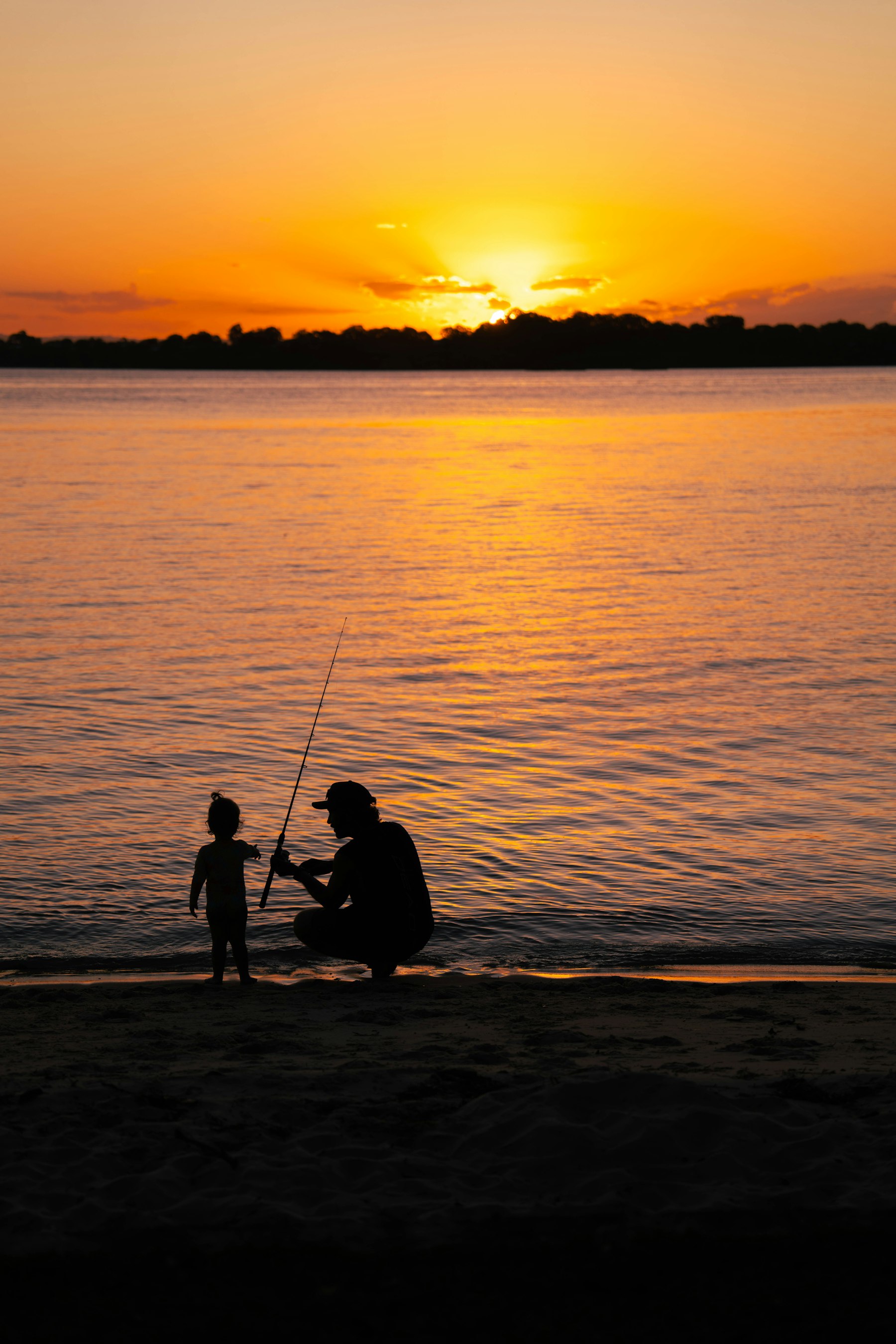 A father teaching his toddler to hold a fishing rod at sunset