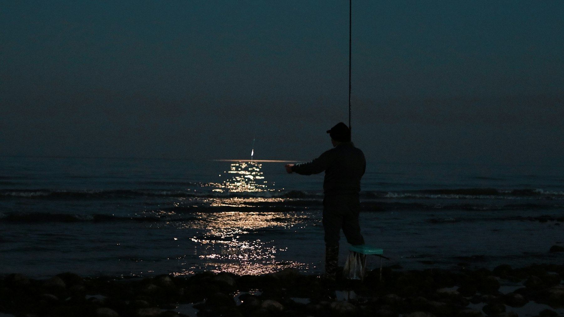 A man fishing the dark ocean at night